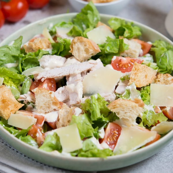 Chicken Caesar salad with lettuce, tomatoes, croutons, parmesan cheese, and dressing in a light green bowl.