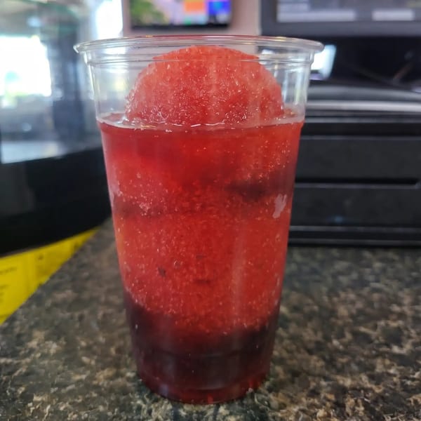 Red slushy drink in a clear plastic cup with a dark red bottom layer.